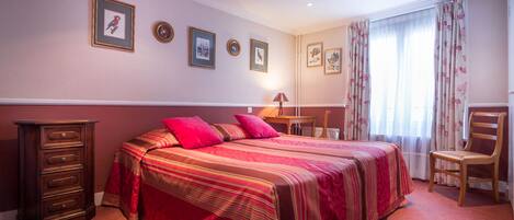 A bedroom with a bed, dresser, chair, and framed pictures on the wall.