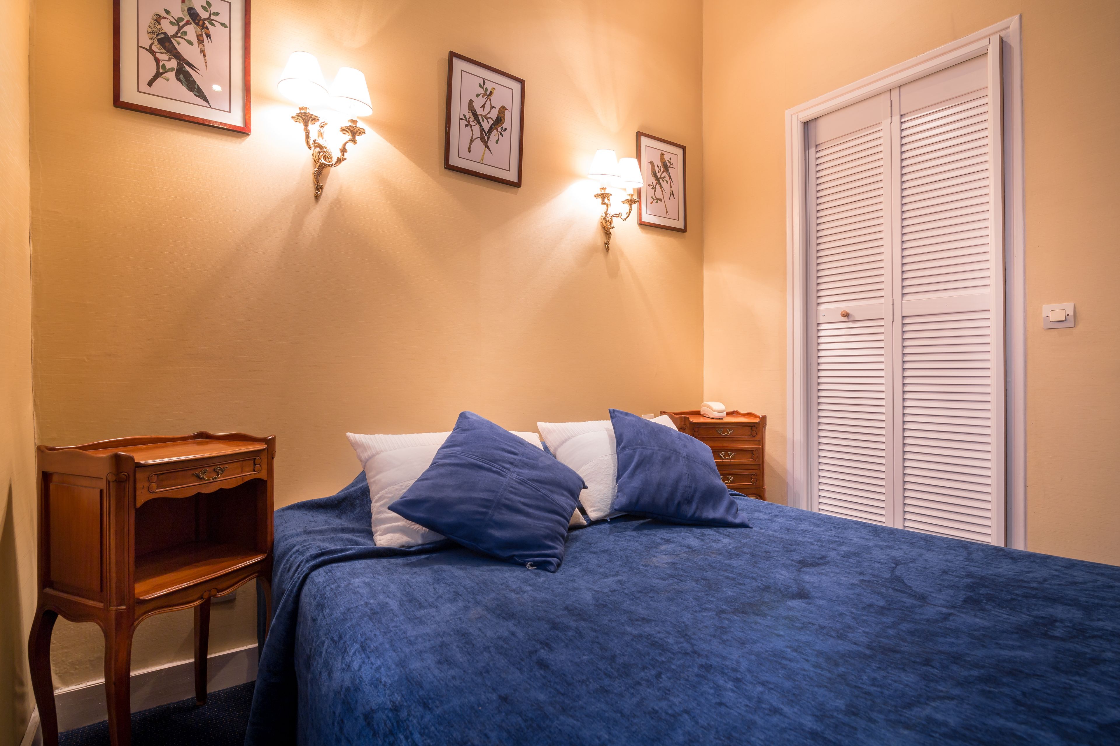 A bedroom with a bed, two wall-mounted lamps, a nightstand, and a closed closet.
