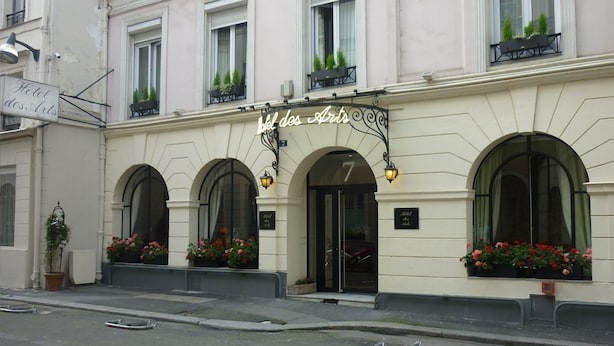 La façade d’un hôtel présente un style architectural classique, avec des fenêtres en arc et une entrée imposante.