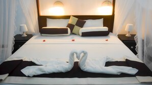 Cama bem arrumada com toalha em formato de coração, duas luminárias de cabeceira e cabeceira com iluminação embutida.