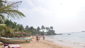 Uma praia com palmeiras, um barco e pessoas relaxando.