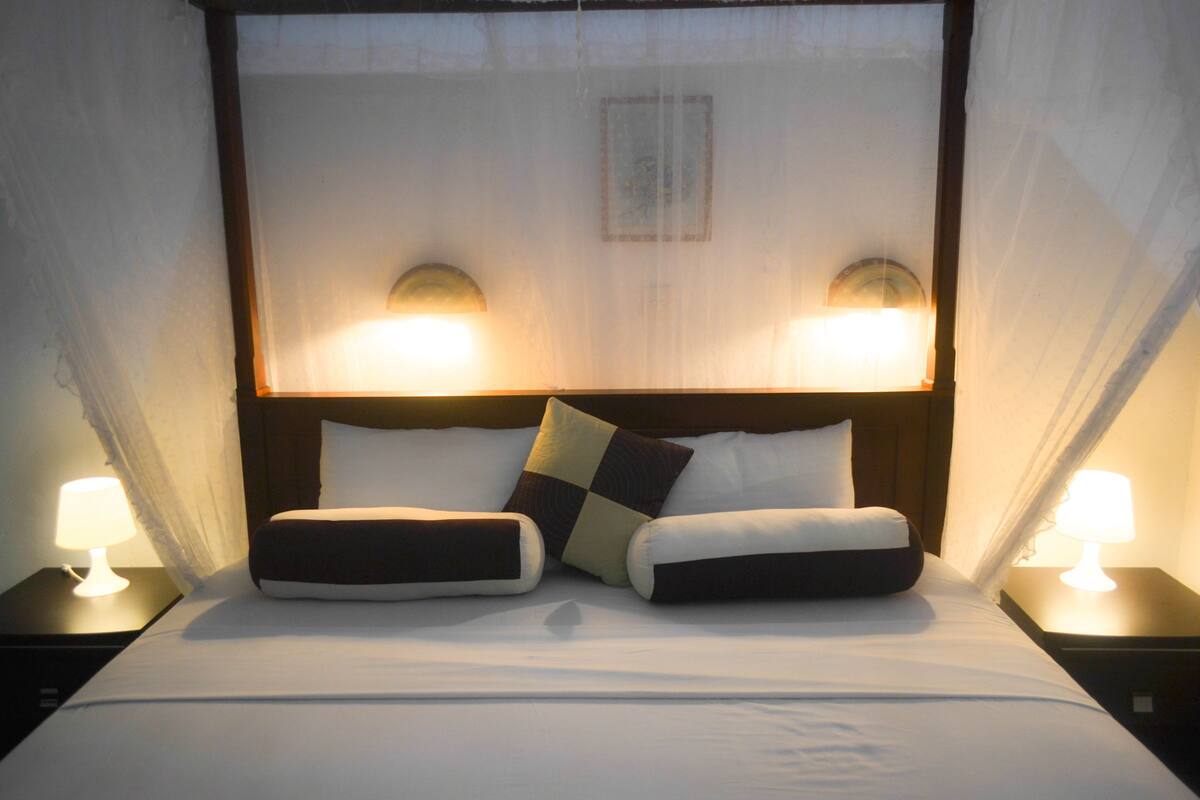 A hotel room with a bed, two bedside lamps, and a canopy bedspread.