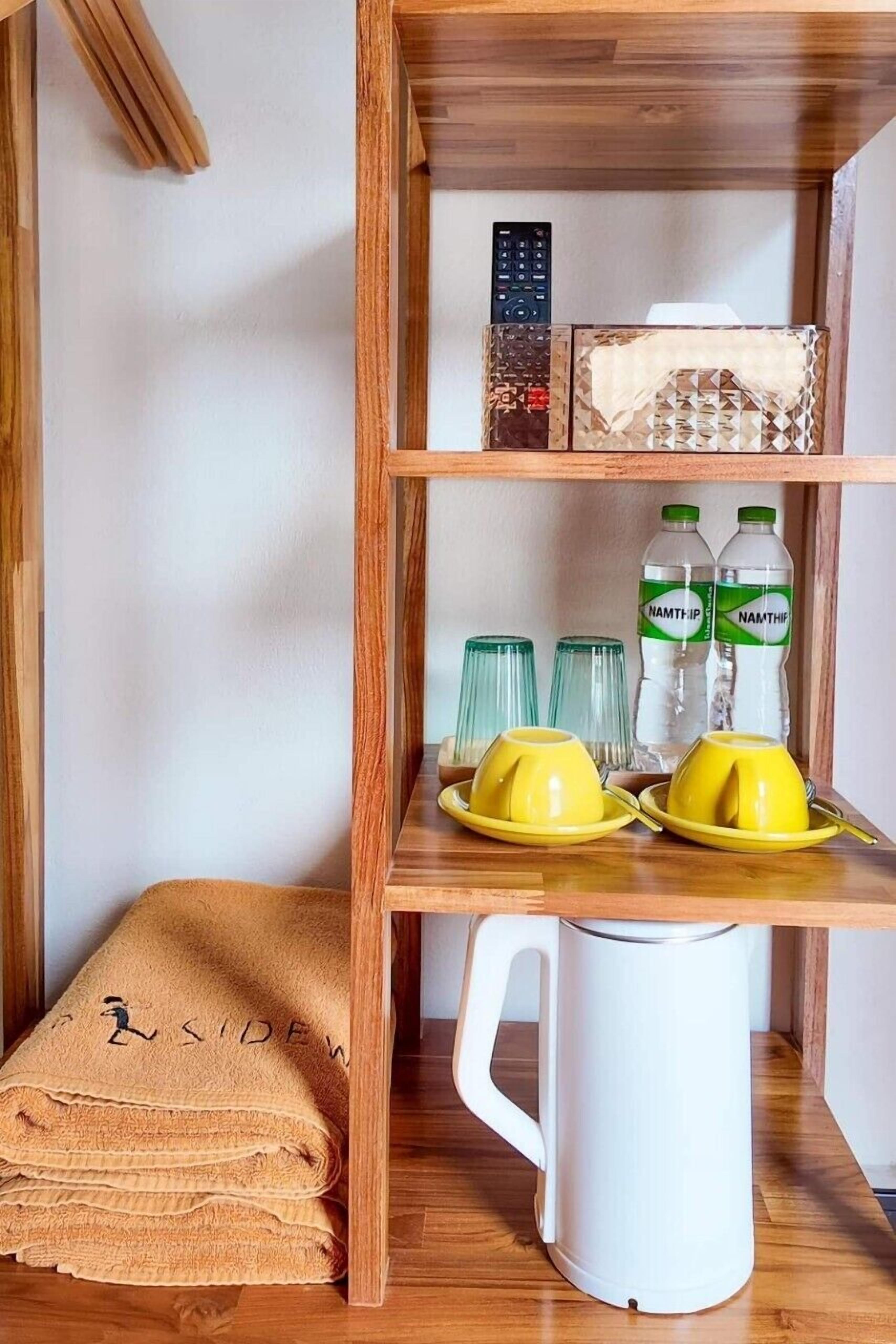 Een houten plank met een afstandsbediening, twee waterflessen, twee glazen en een witte waterkoker.