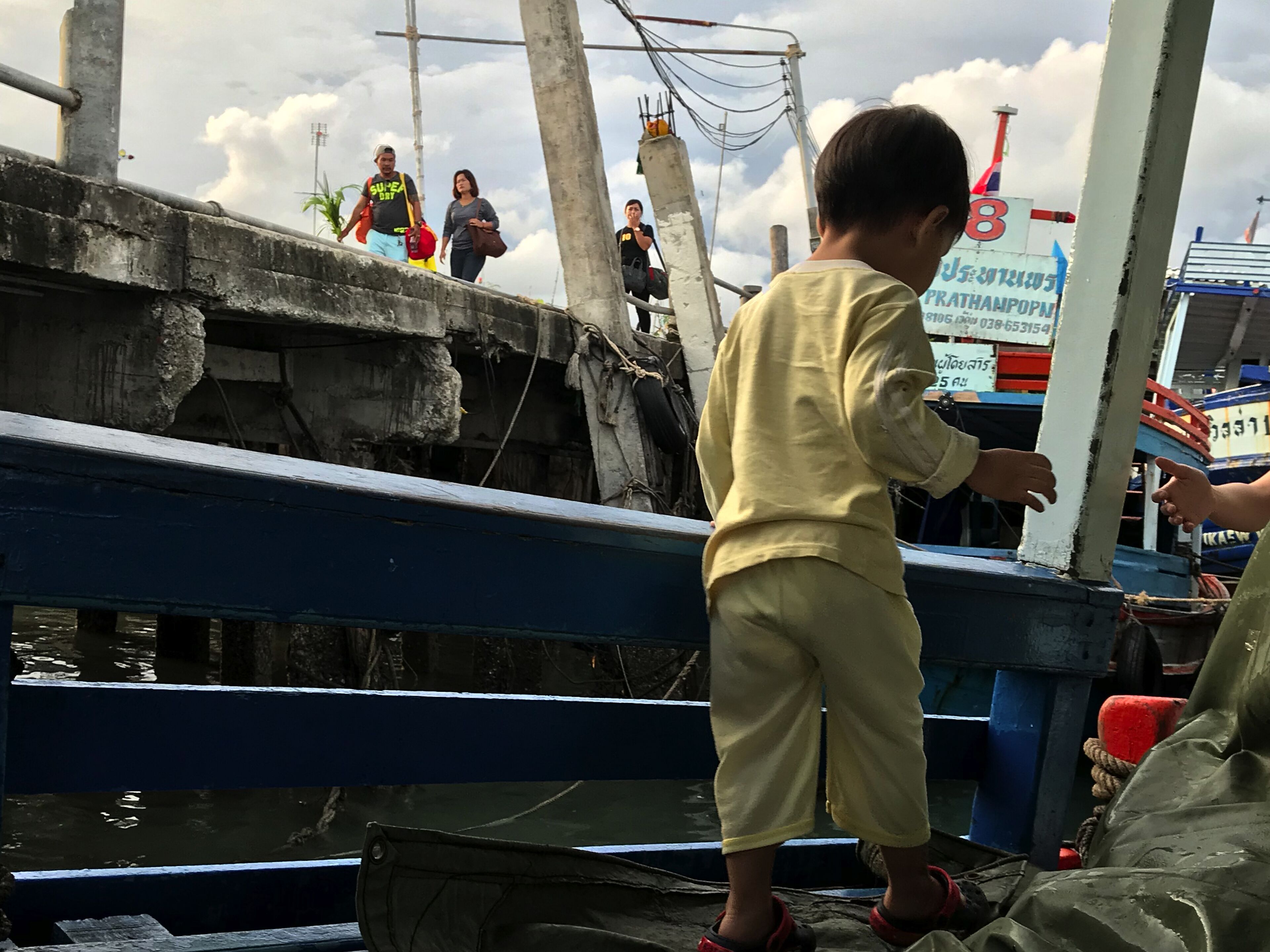 Un enfant se tient sur un quai, avec un bateau en arrière-plan.