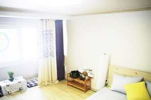 A room with a bed, a bedside table with a fan, a small plant, and a checkered tablecloth.