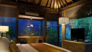 A room with a bed, a TV, a desk, and a window with a view of greenery. - Komea Villa (Canggu)