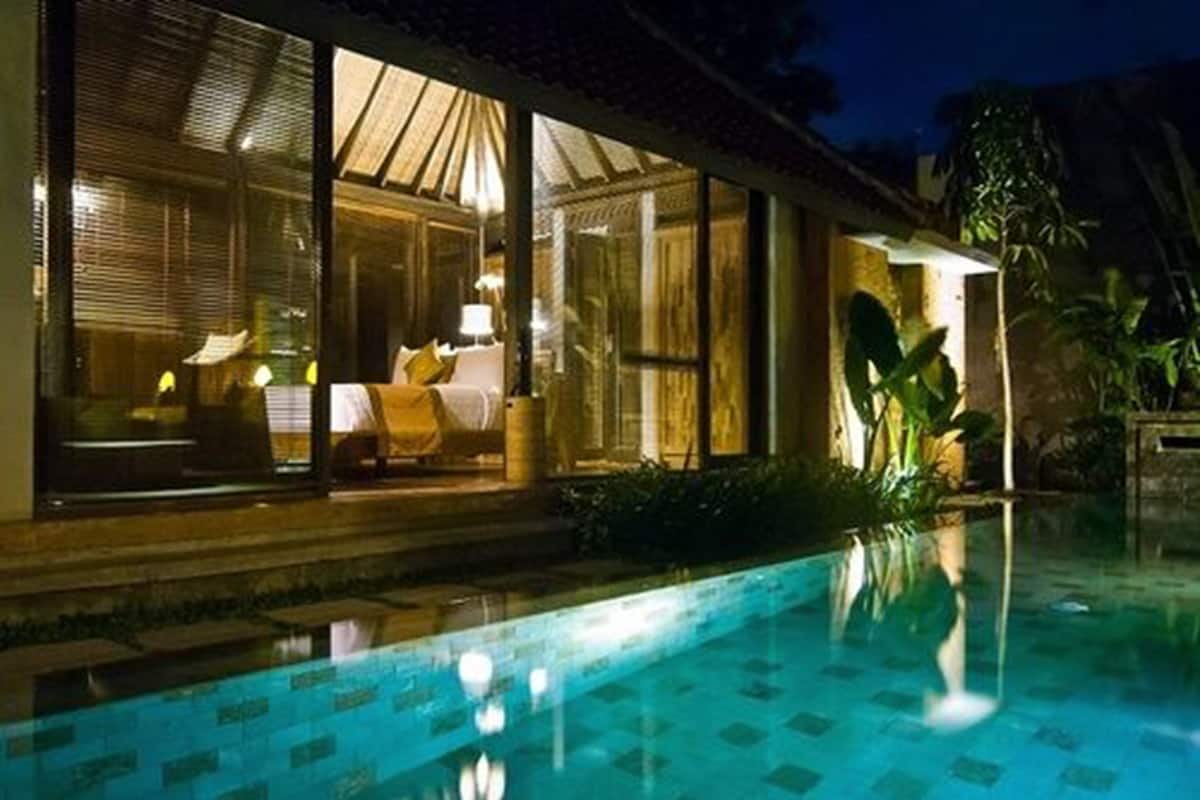 A poolside view of a hotel room with a bed, a window, and a view of the pool.