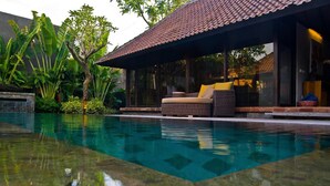A swimming pool with a clear water surface, surrounded by lush greenery and a covered seating area with cushions. - Komea Villa (Canggu)