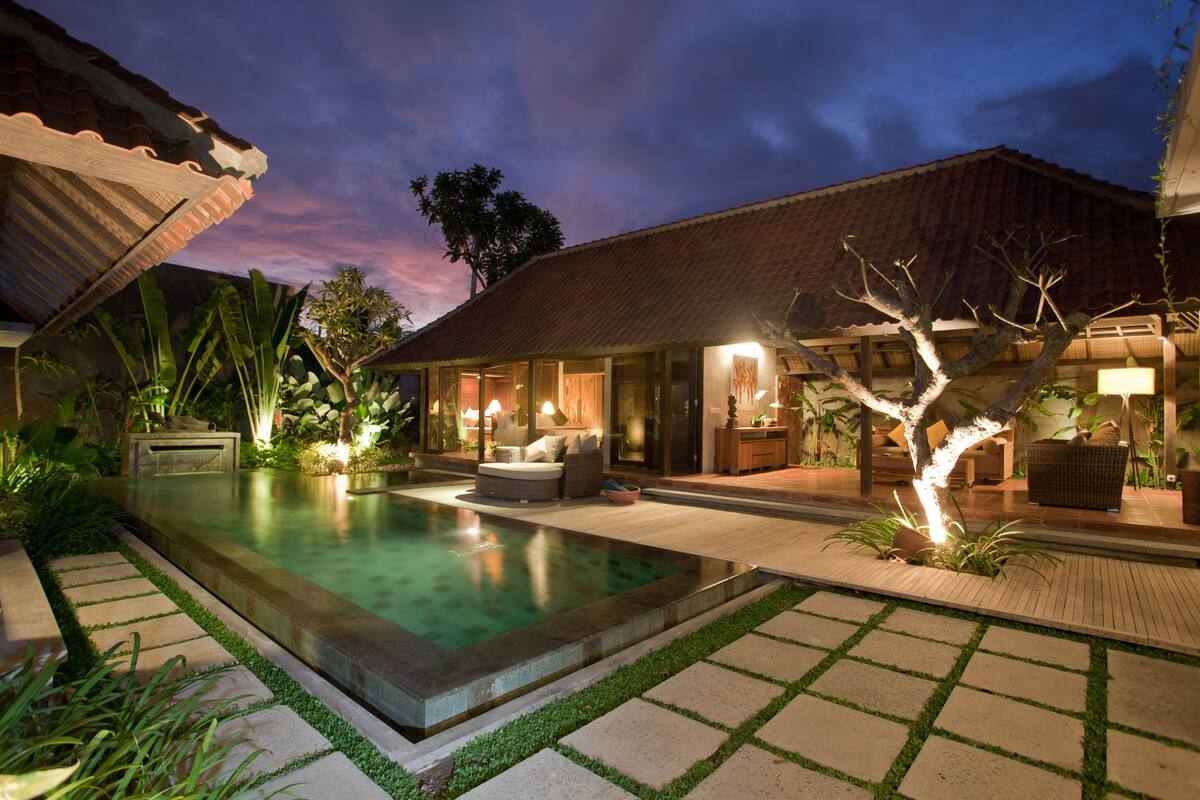 A poolside area with a swimming pool, outdoor furniture, and a well-lit patio.