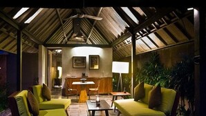 A cozy room with a high ceiling, a dining table, and two green sofas. - Komea Villa (Canggu)