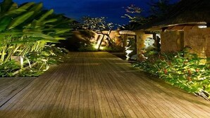 A wooden pathway leading to a building with a thatched roof, surrounded by lush greenery. - Komea Villa (Canggu)
