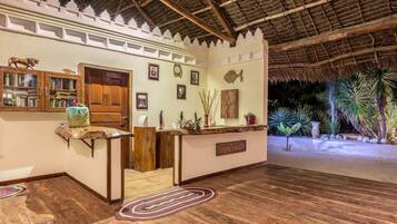 Una habitación con piso de madera, techo de paja y una recepción con cuadros enmarcados y una planta pequeña.