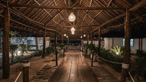 A covered wooden walkway with hanging lights, surrounded by potted plants and a rustic thatched roof structure. - Hakuna Majiwe Beach Lodge (Paje)