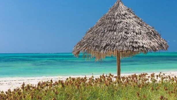 A beach scene with a thatched umbrella and clear turquoise waters. - Hakuna Majiwe Beach Lodge (Paje)