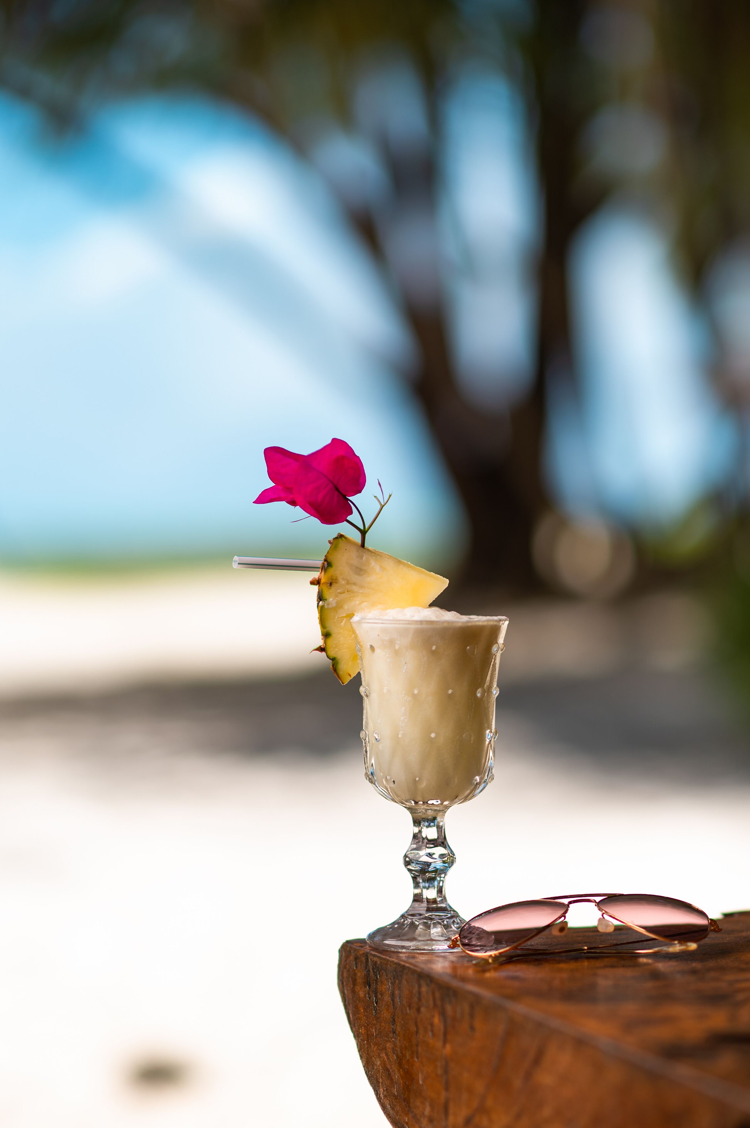 Un vaso con una rodaja de piña y una flor rosa sobre una superficie de madera.