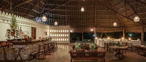 Un espacio interior con techo de madera alto, una zona de bar con taburetes y un área de estar con mesas y bancos.