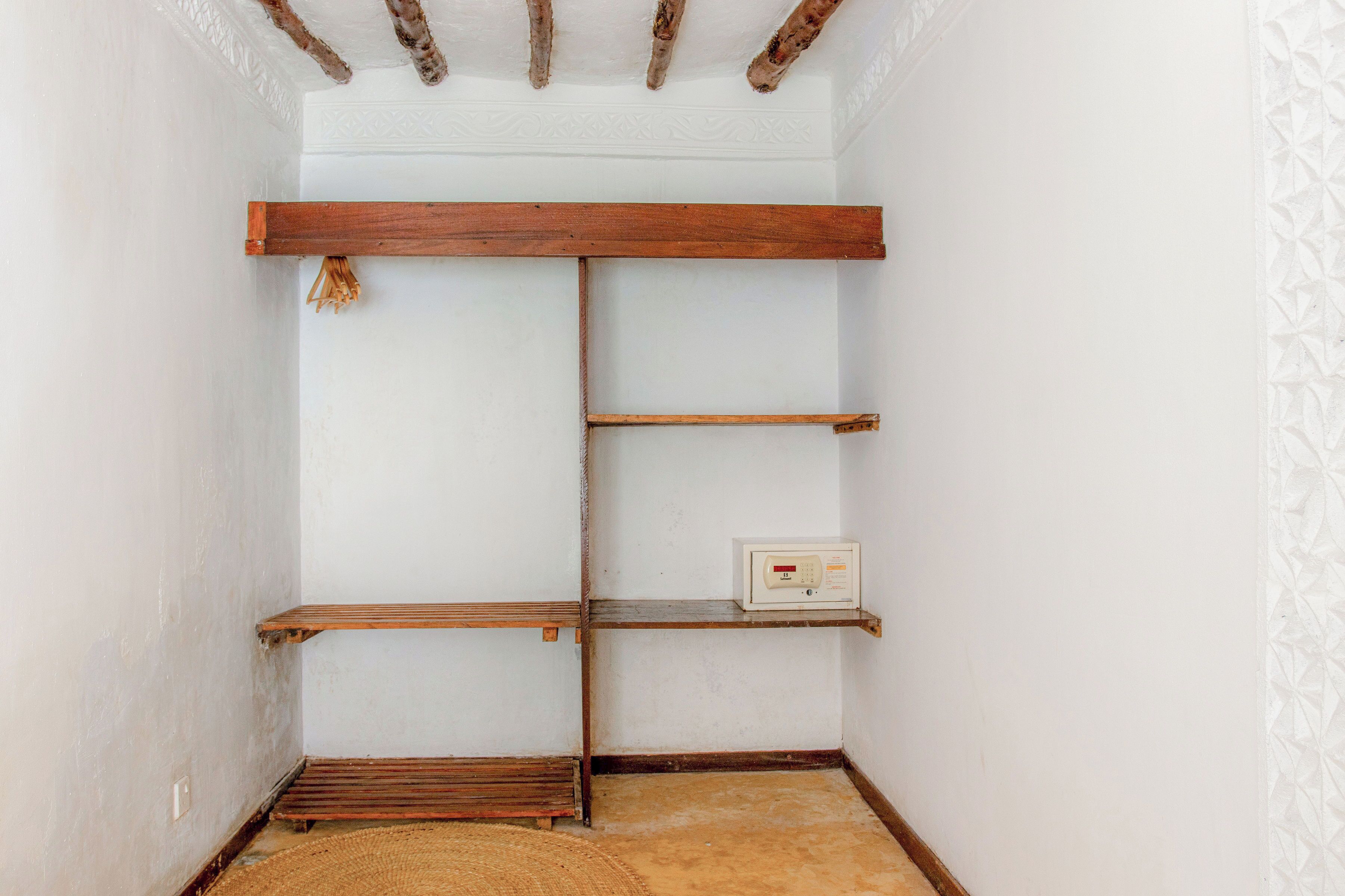 A room with a wooden beam ceiling, a built-in shelf, and a thermostat on the wall.