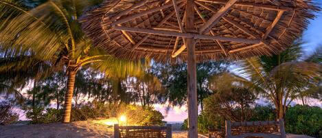 A beach with a thatched umbrella and wooden benches.