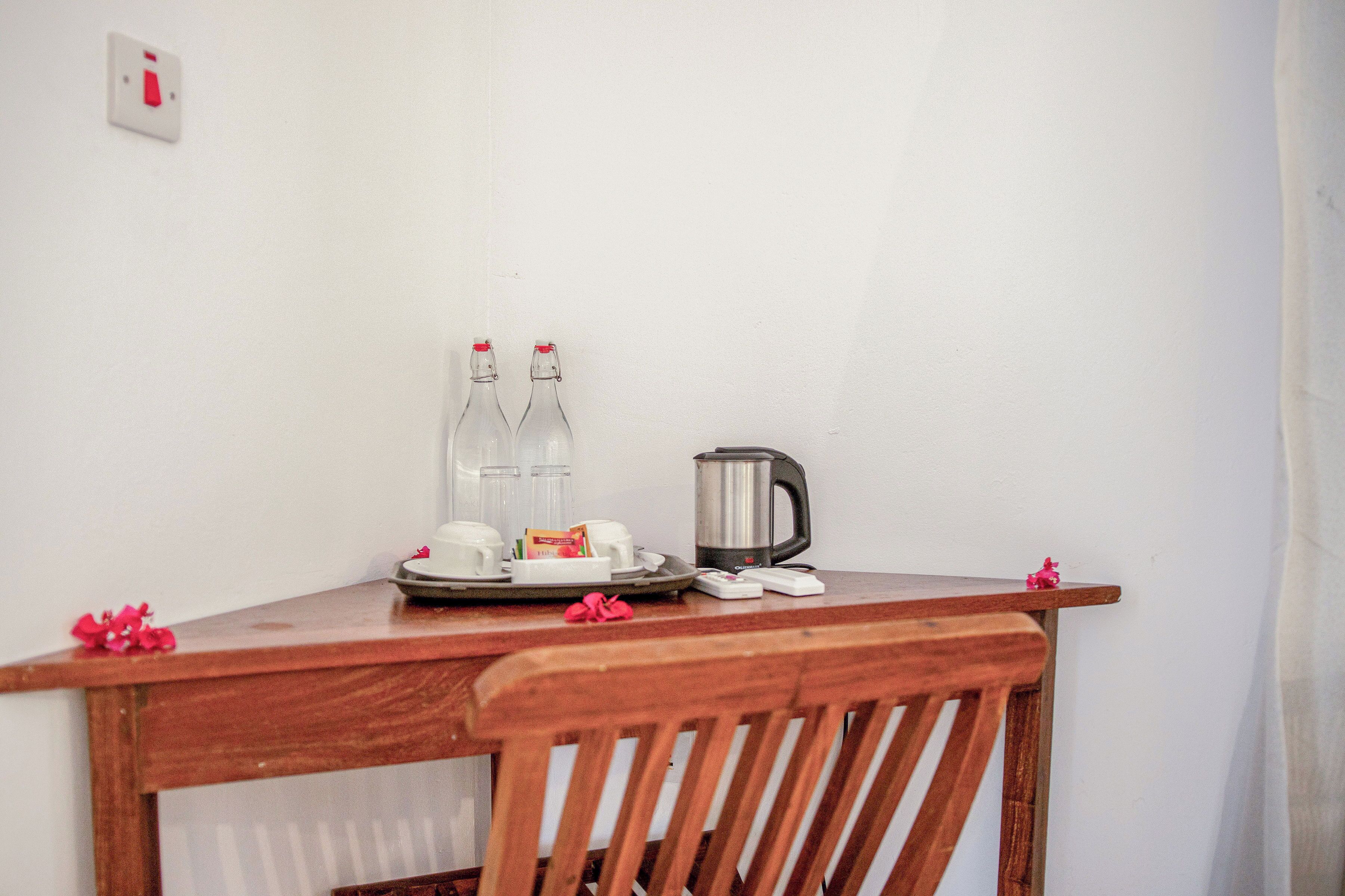 Une table en bois avec une bouilloire, deux bouteilles, des tasses et un plateau sur lequel se trouve un petit objet.