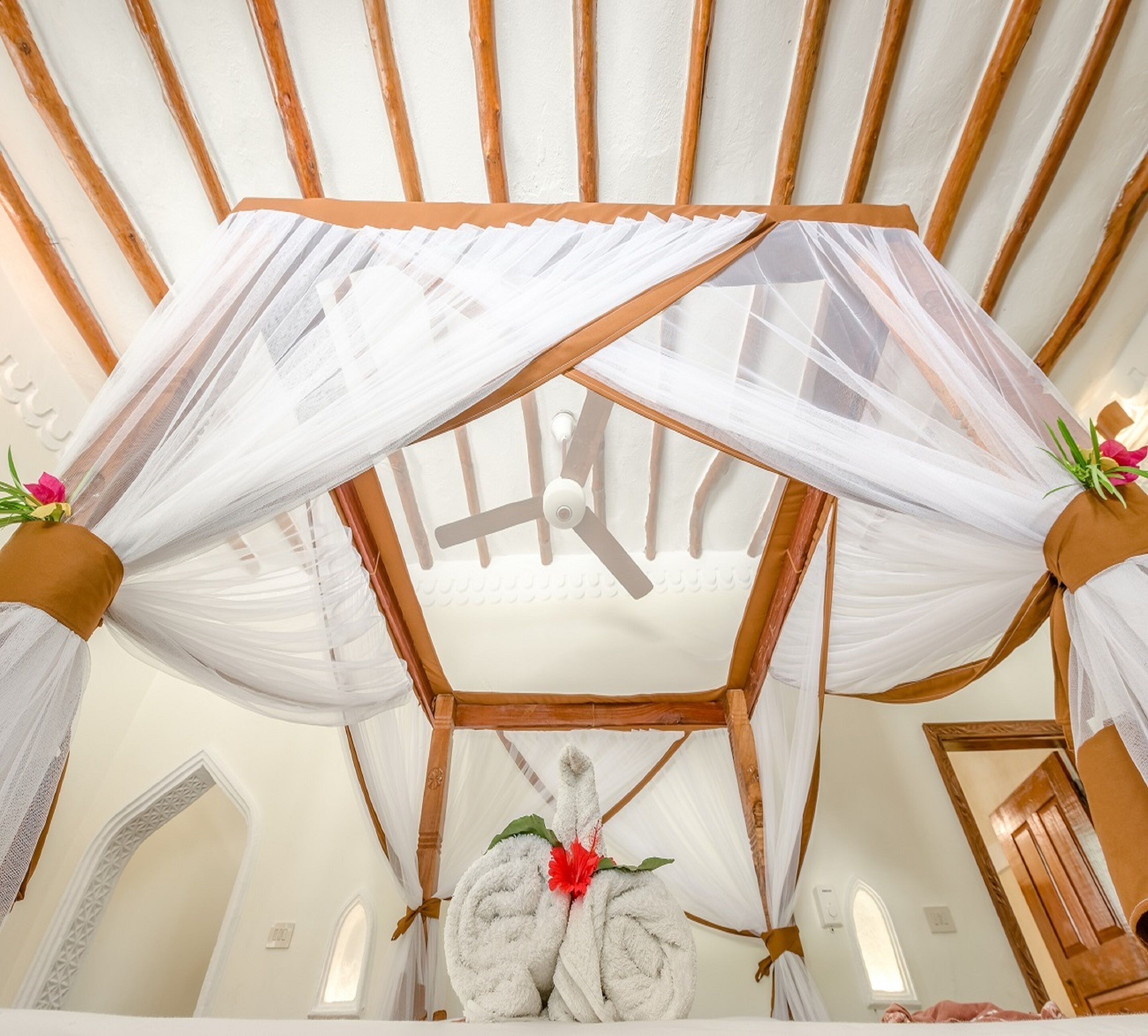 A room with a wooden ceiling and a white canopy bed with a ceiling fan.