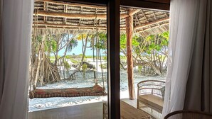 A room with a view of a beach, a thatched roof structure, and wicker furniture. - Hakuna Majiwe Beach Lodge (Paje)
