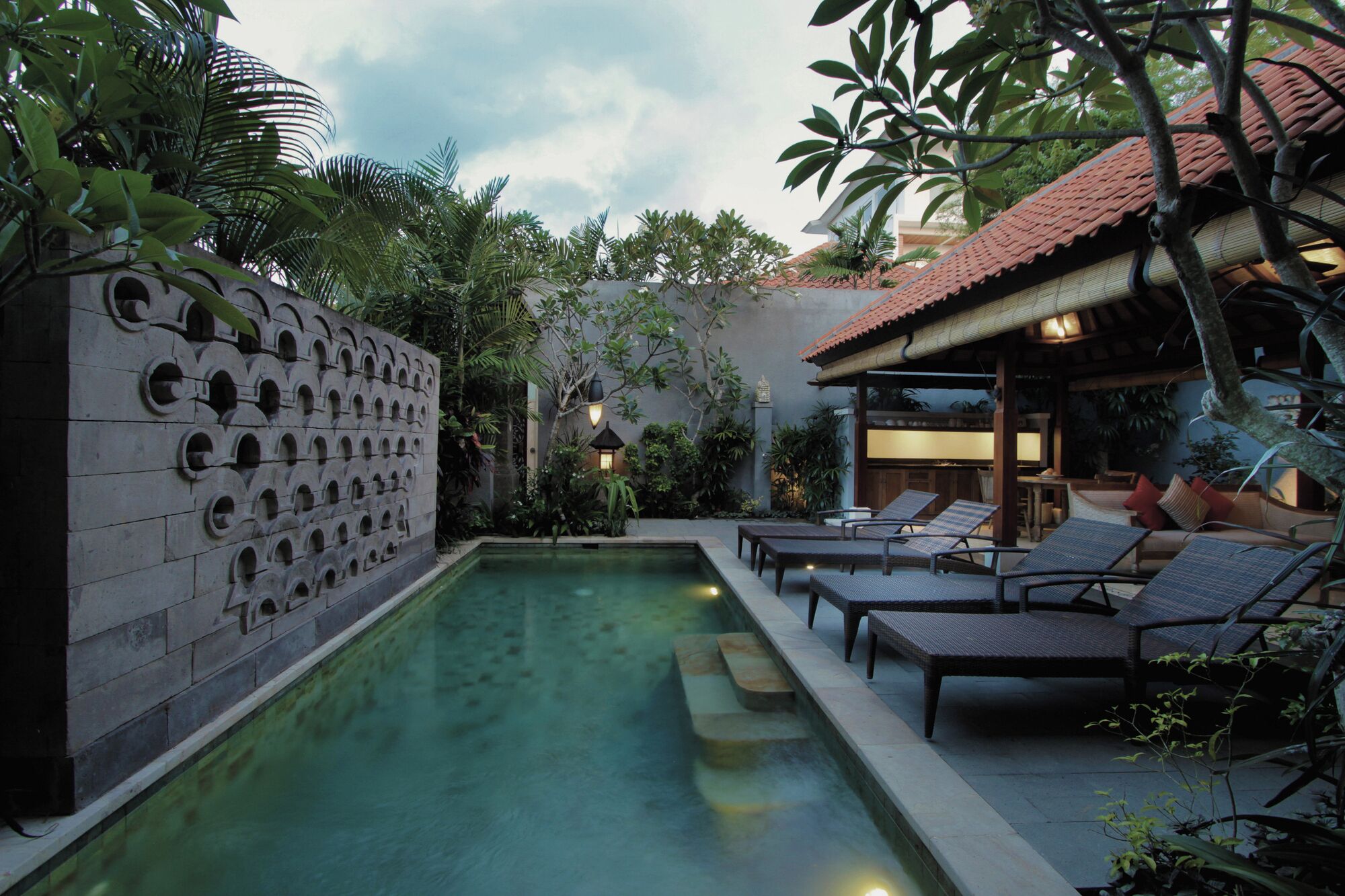 A pool area with lounge chairs and a stone wall with circular cutouts.