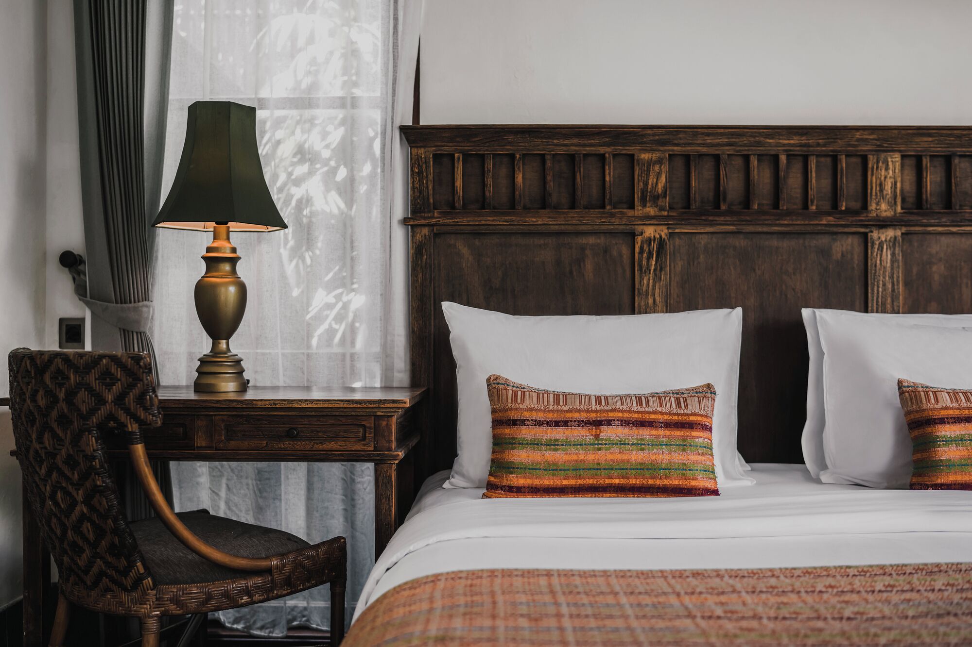 Una camera d'albergo con una testiera in legno, un comodino con una lampada, una sedia e due cuscini a righe.