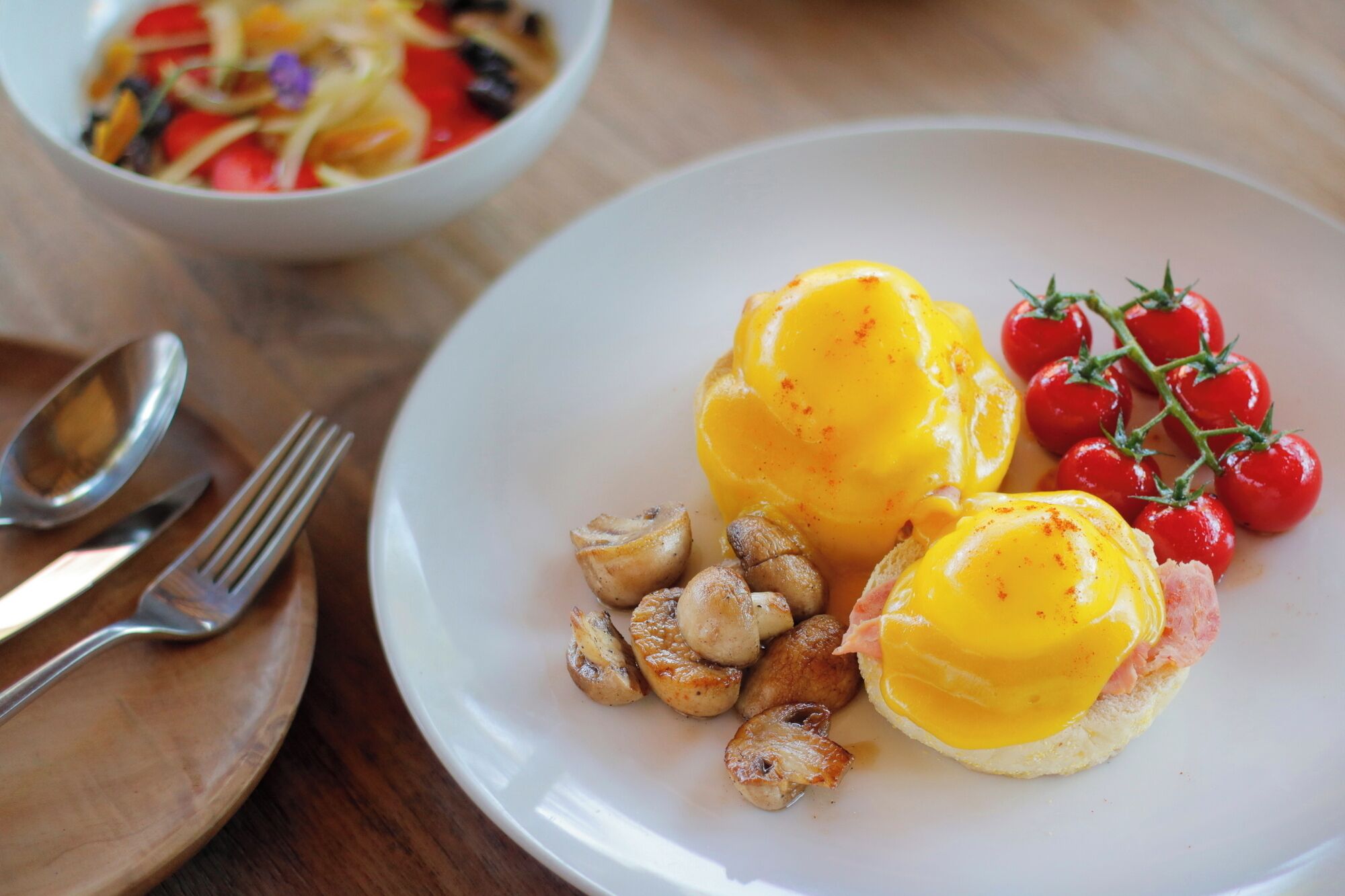 Un plato con huevos Benedict, tomates cherry y setas asadas.