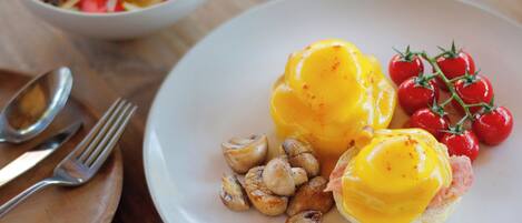 Un plato con huevos Benedict, tomates cherry y setas asadas.