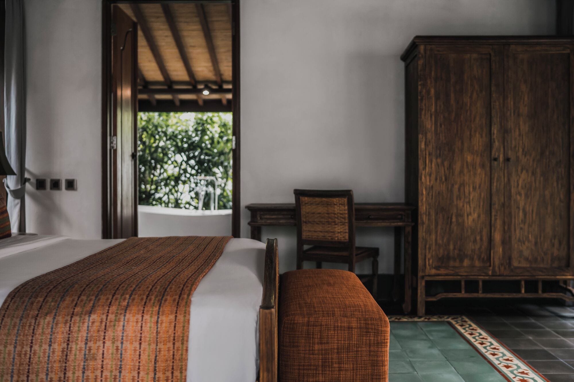 A bedroom with a bed, a wooden cabinet, and a view of greenery outside.