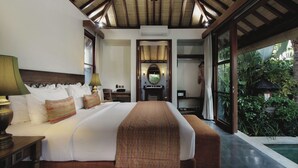 Une chambre spacieuse avec un grand lit, une table de chevet, un bureau et une vue sur un jardin luxuriant, visible à travers une porte vitrée.