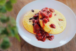 Two pancakes on a white plate with a red sauce on top.