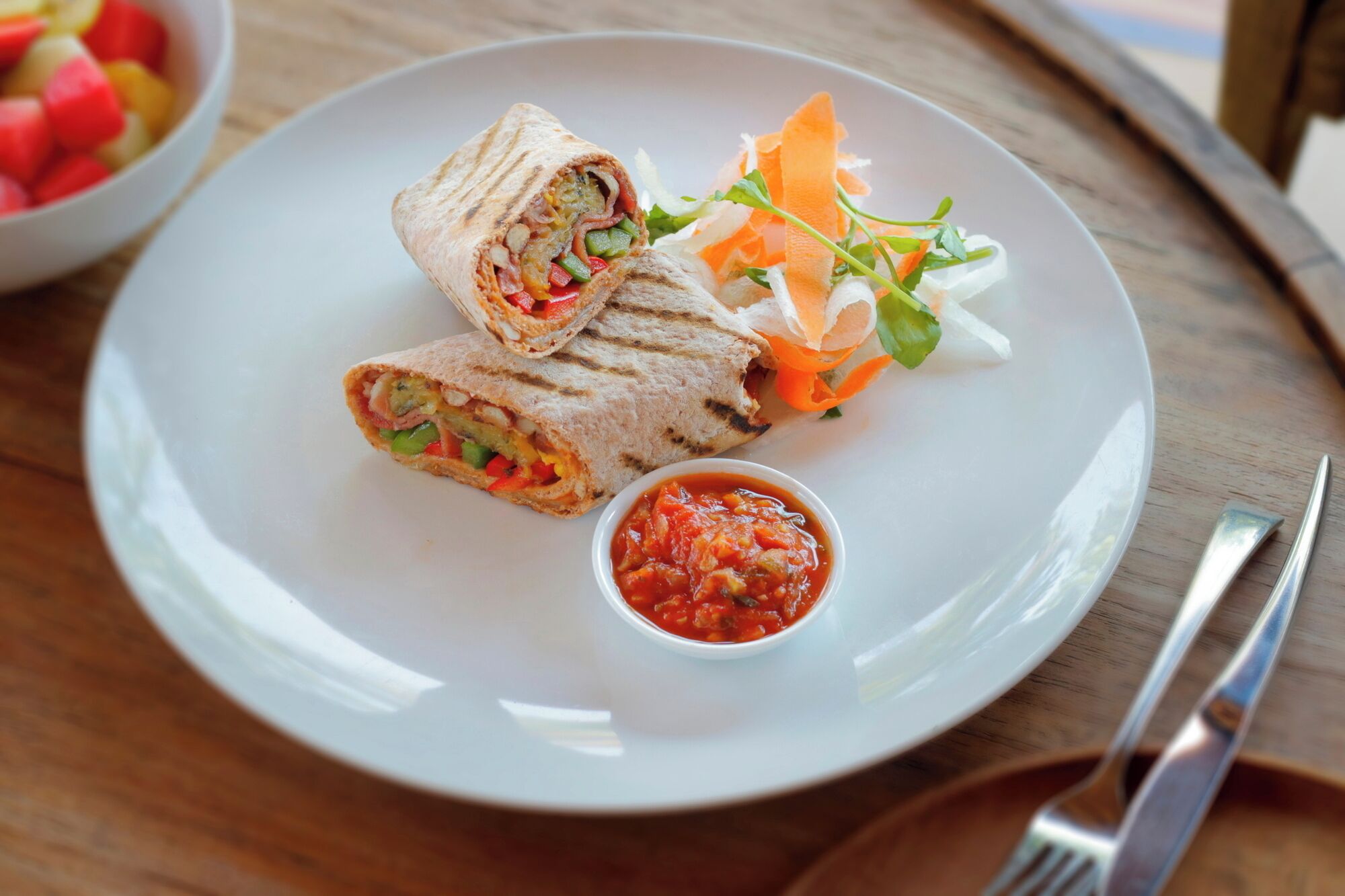 Une assiette avec un wrap, un petit bol de sauce et une salade en accompagnement.