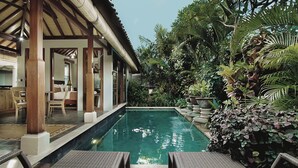 Un espace piscine agrémenté de chaises longues, d’une pergola en bois et d’une végétation tropicale luxuriante.