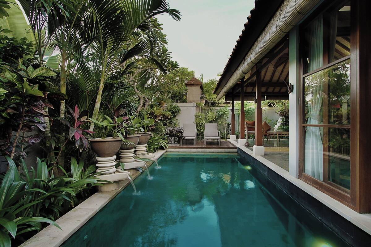 Una piscina rodeada de exuberante vegetación tropical y una estructura de madera tradicional.