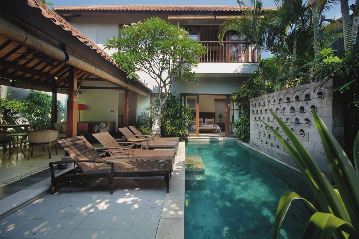Zona de piscina con sillones reclinables, una piscina pequeña y un edificio con balcón.