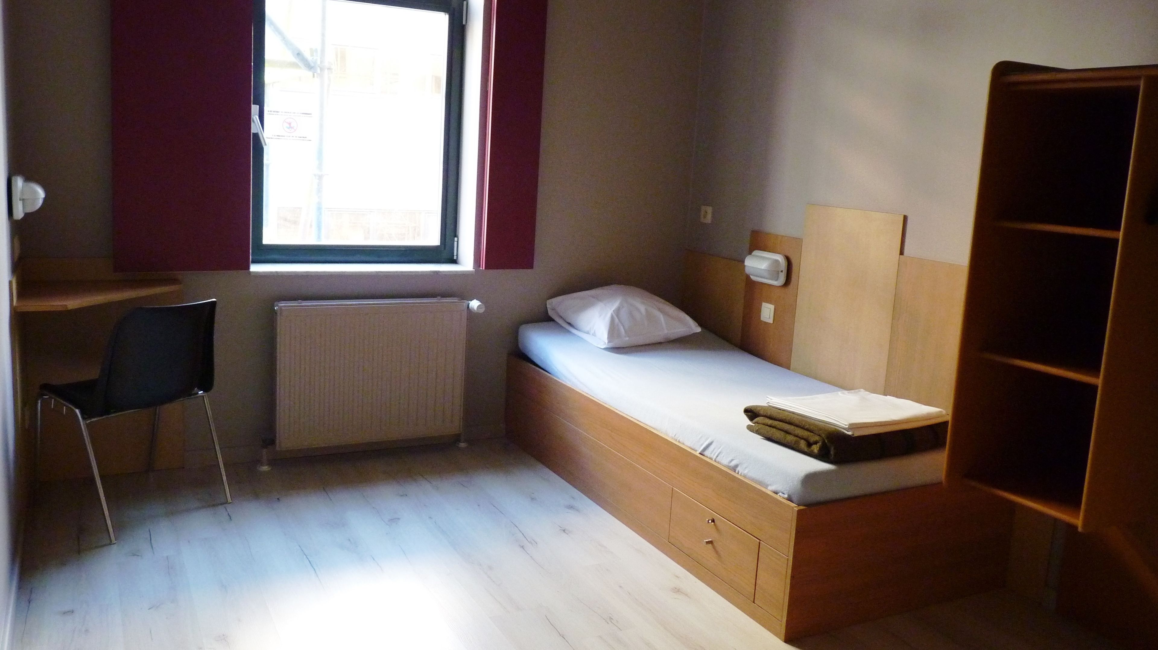 Une petite chambre avec un lit simple, un bureau et une chaise.