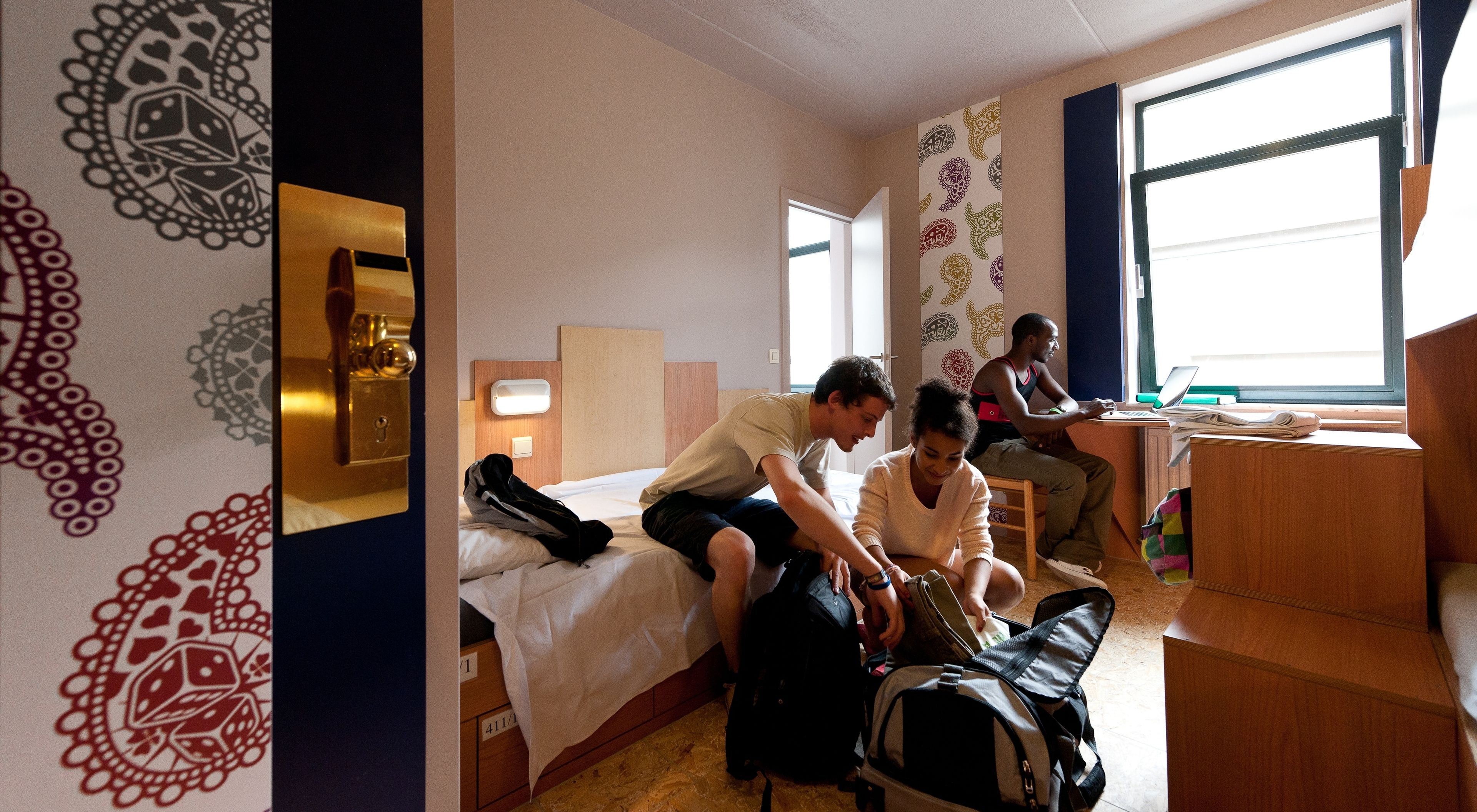 A hotel room with a bed, a desk, and a window.
