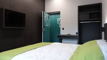 Una habitación de hotel con una cama, televisión montada en la pared, armario y un escritorio pequeño con espejo.