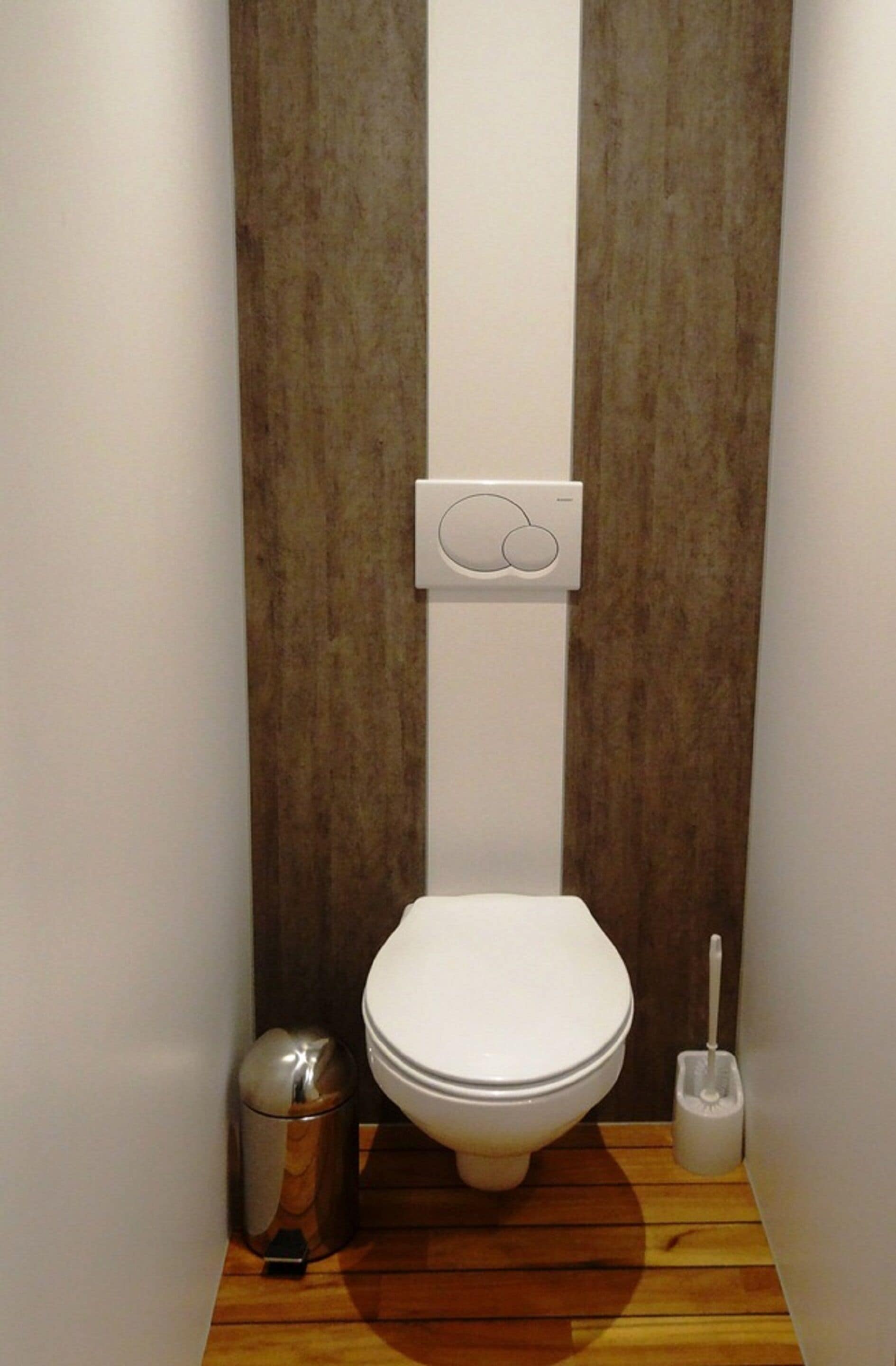 Uma casa de banho compacta com sanita branca, um cesto de lixo e uma escova de sanita.
