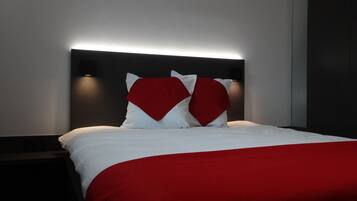 Een moderne hotelkamer met een opgemaakt bed, een donker hoofdbord en een rood accentkussen.