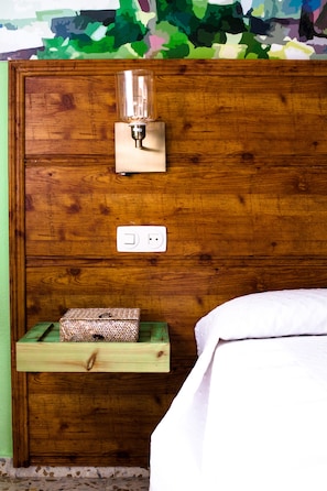 Cabecera de madera con lámpara de noche, enchufe y estante de madera pequeño con una caja estampada.