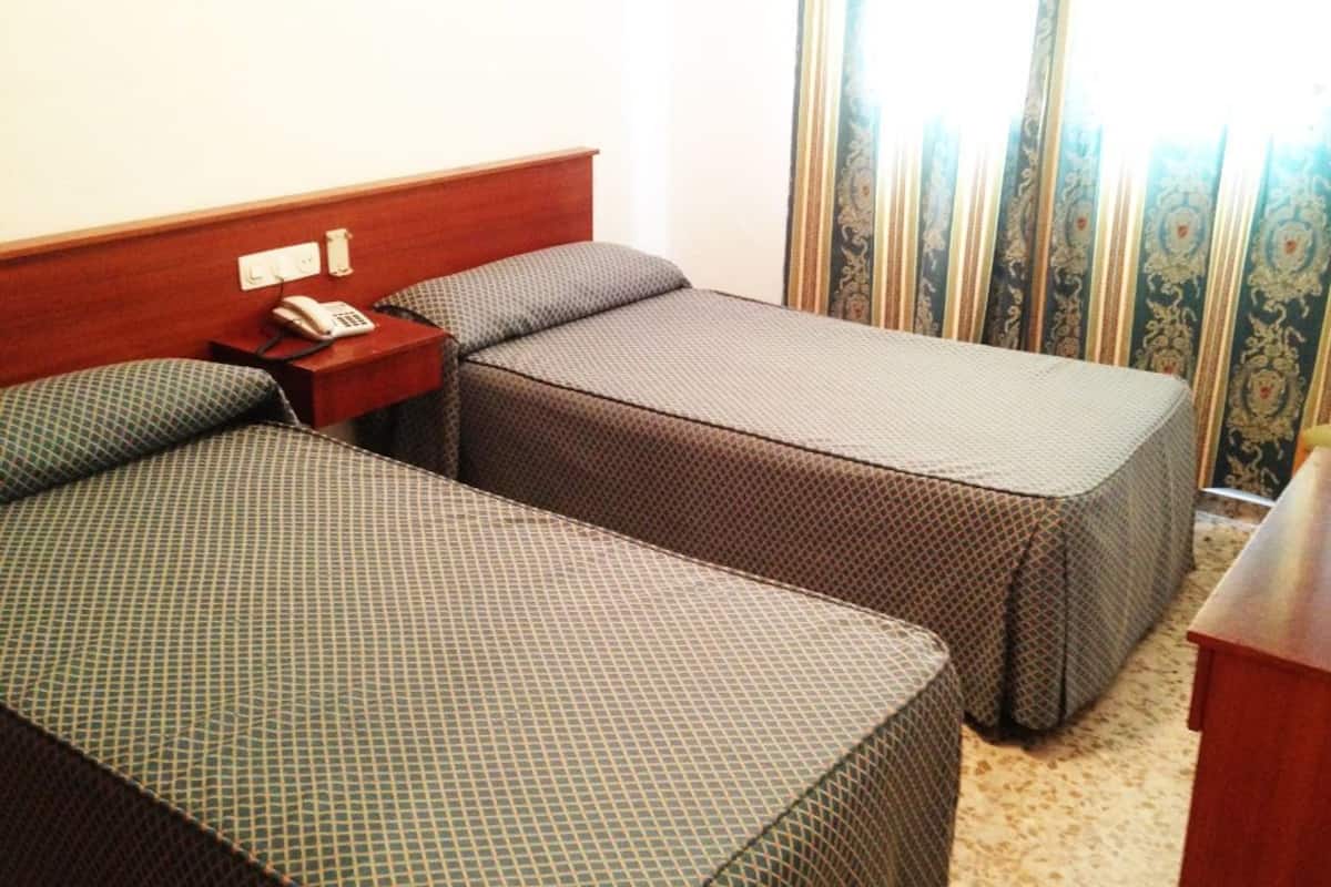 A hotel room with two single beds, a wooden headboard, a bedside table with a phone, and a curtain with a floral pattern.