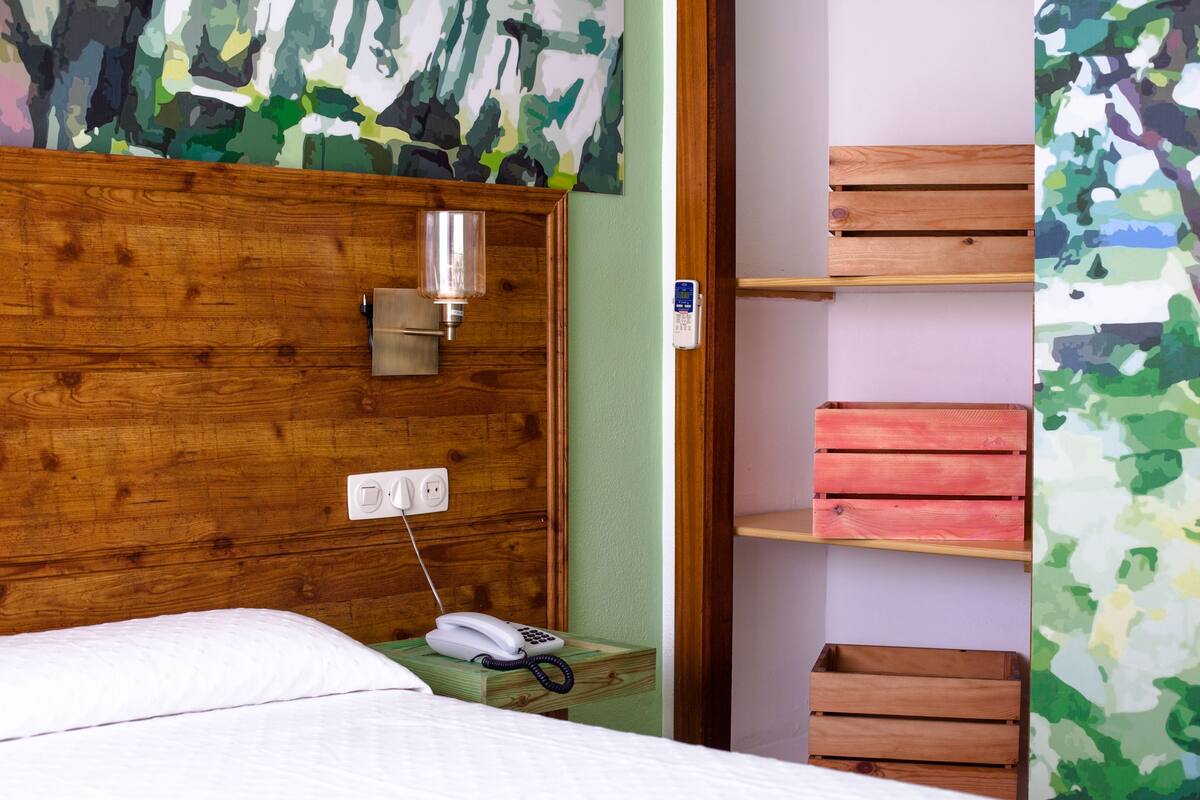 A room with a wooden headboard, a bedside telephone, a nightstand, and a shelf with wooden crates.