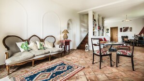 A spacious living room with a sofa, chairs, a patterned rug, and a staircase leading to another area. - Nake Residenza Artistica (Sant'Alfio)