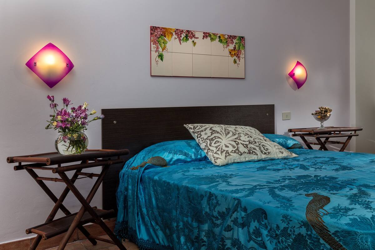 A bedroom with a bed, two nightstands, a wall-mounted light fixture, and a decorative wall piece.