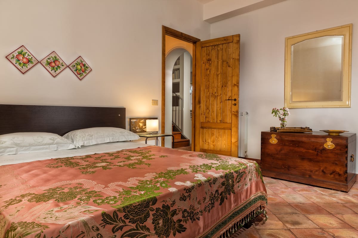 A bedroom with a bed, a wooden wardrobe, a mirror, and three wall-mounted pictures.