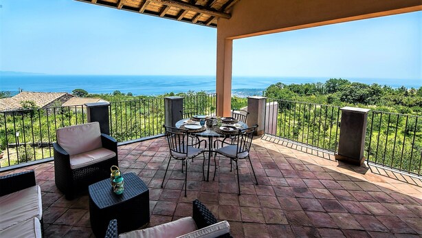 A terrace with a table set for dining, outdoor seating, and a view of the sea. - Nake Residenza Artistica (Sant'Alfio)