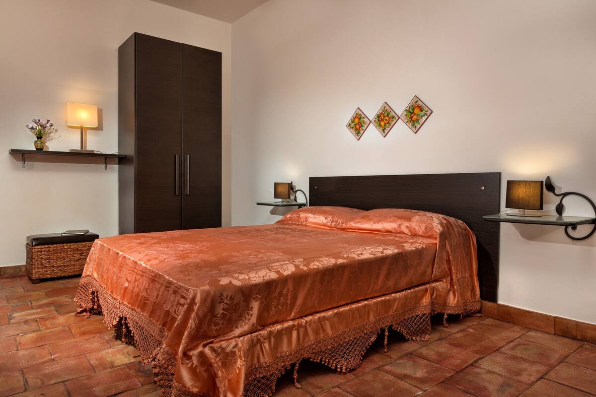 A bedroom with a large bed, two bedside tables with lamps, a wardrobe, and decorative wall art.
