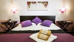 A neatly made bed with purple and white bedding, two nightstands with lamps, and a wall-mounted artwork above the bed. - Nake Residenza Artistica (Sant'Alfio)